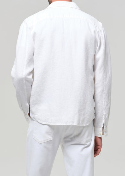 Person wearing a white linen shirt and pants against a plain background