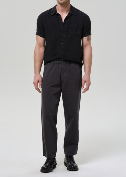 Man wearing a black button-up shirt and pants on a grey background.