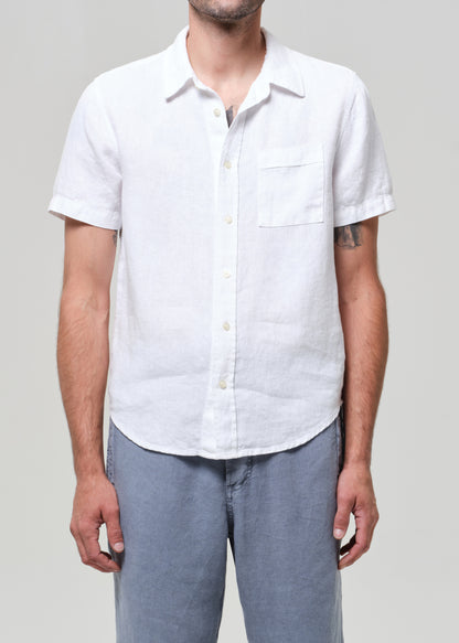 Man wearing a white linen short-sleeve shirt and light gray linen pants on a plain background