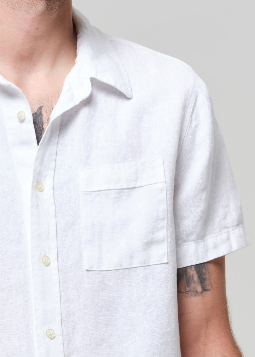 White short-sleeve shirt worn by a person with tattoos on a plain background