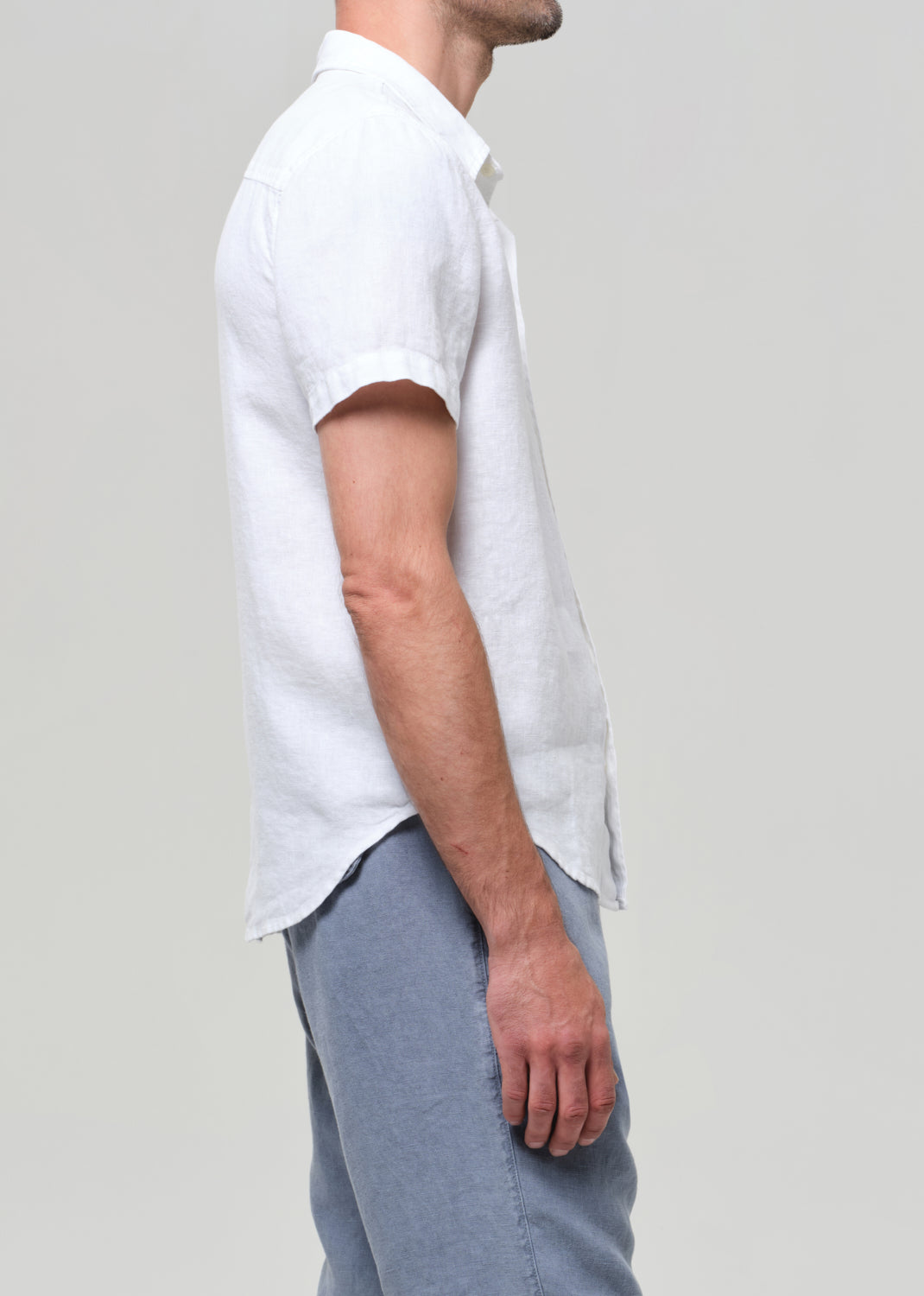 Man wearing a white linen short-sleeve shirt and light gray linen pants on a plain background