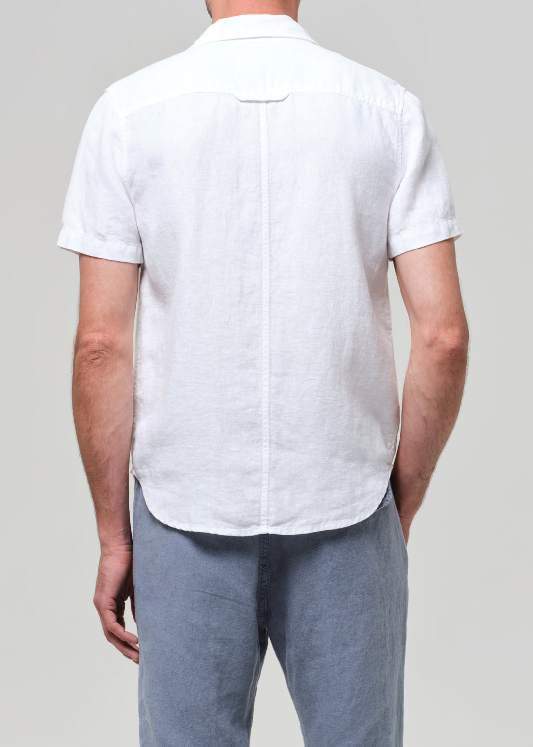 Man wearing a white linen short-sleeve shirt and light gray linen pants on a plain background
