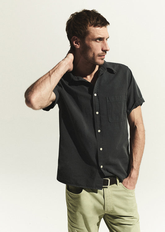 Man wearing a grey short-sleeve shirt and light green pants against a plain background