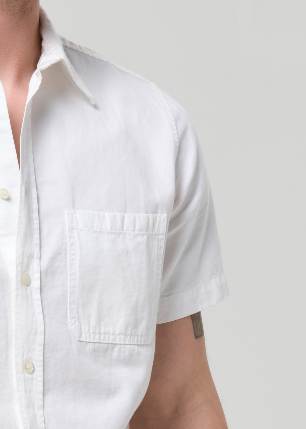 Close-up of a person wearing a white short-sleeve button-up shirt with a chest pocket, against a grey background.