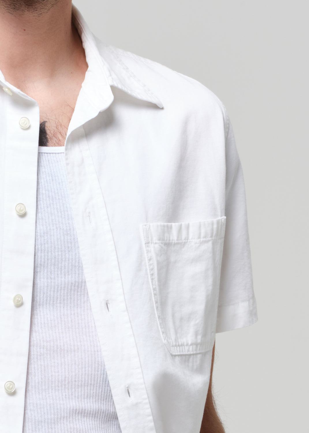 Man wearing a white shirt and dark jeans against a grey background