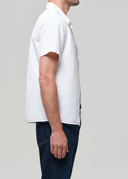 Man wearing a white shirt and dark jeans against a grey background