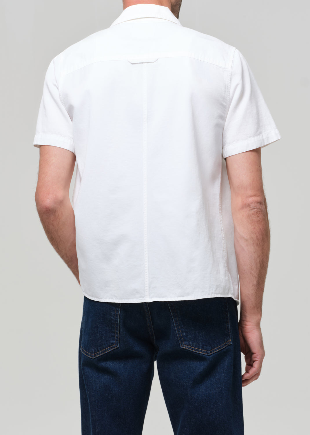 Man wearing a white shirt and dark jeans against a grey background