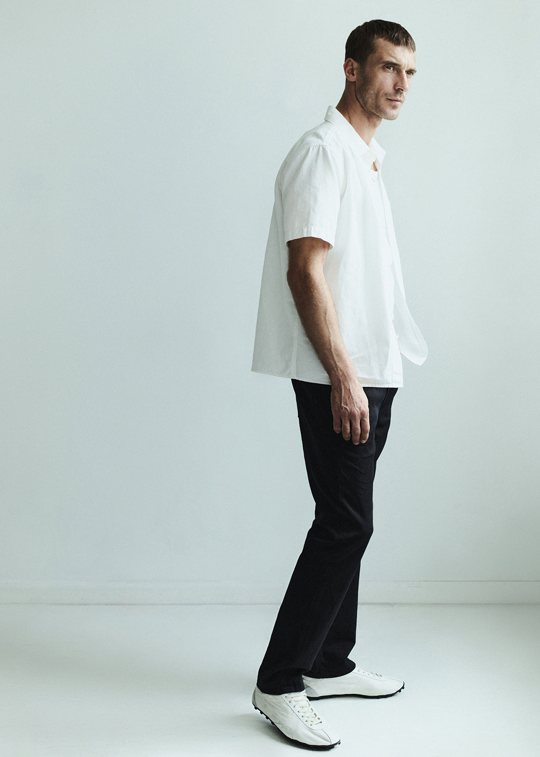 Man wearing a white shirt and dark jeans against a grey background