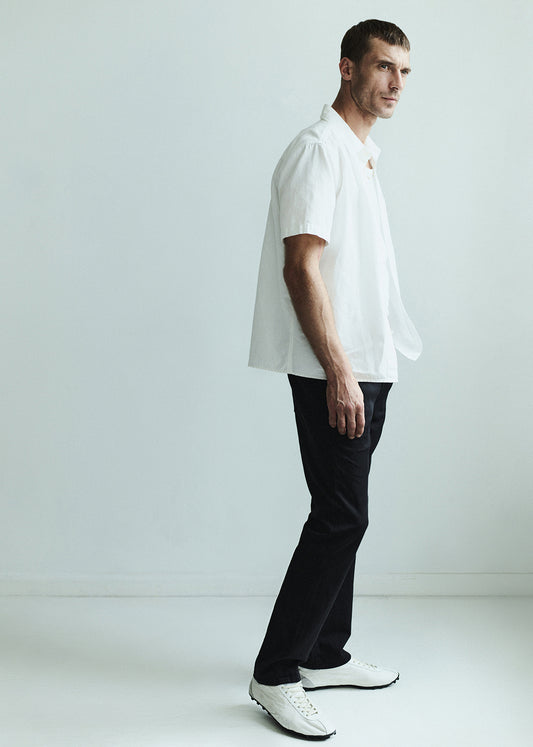 Man wearing a white shirt and dark jeans against a grey background