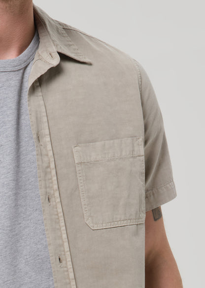 Close-up of a light beige short sleeve button-up shirt on a grey background.