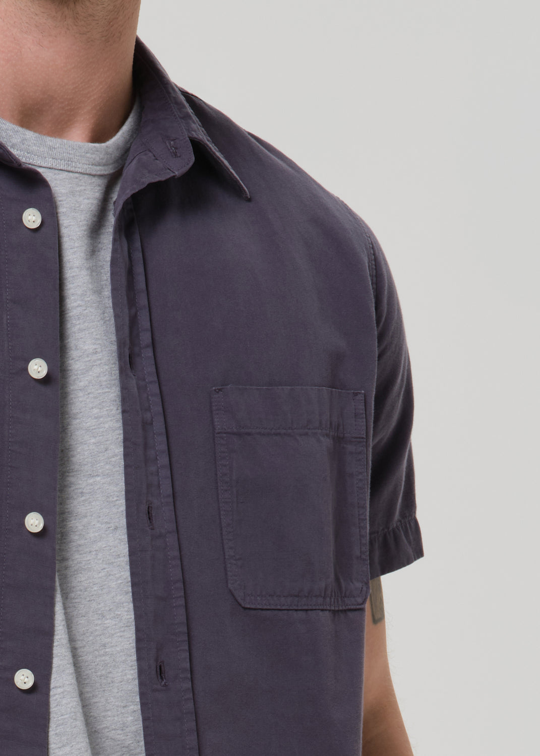 Close-up of a person wearing a dark navy short-sleeve button-up shirt over a light gray crew-neck t-shirt, against a grey background.