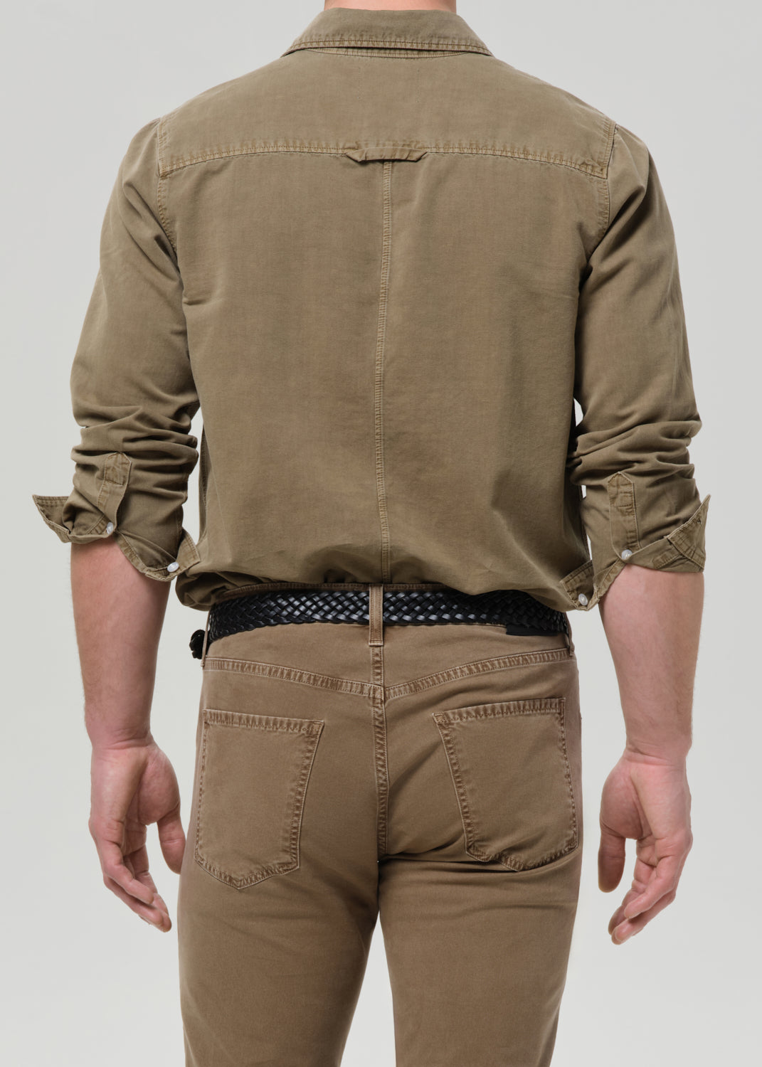 Person wearing a brown shirt and pants on a grey background
