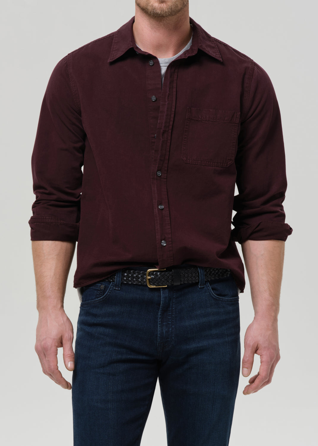 Man wearing a maroon button-up shirt and dark jeans on a grey background