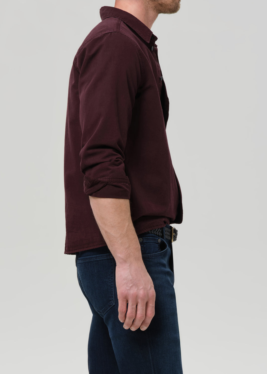 Man wearing a maroon long-sleeve shirt and dark jeans on a grey background