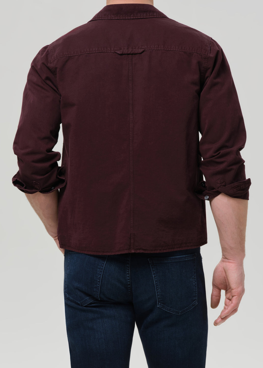 Person wearing a maroon shirt and dark jeans on a grey background