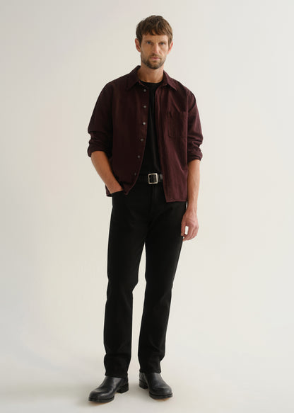 Person wearing a dark burgundy button-up shirt over a black shirt with black pants and black shoes, front full body view on a light grey background.