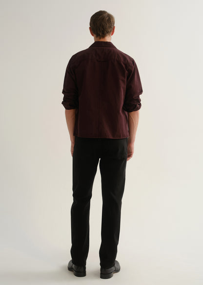 Person wearing a dark burgundy button-up shirt with black pants and black shoes, back full body view on a light grey background.