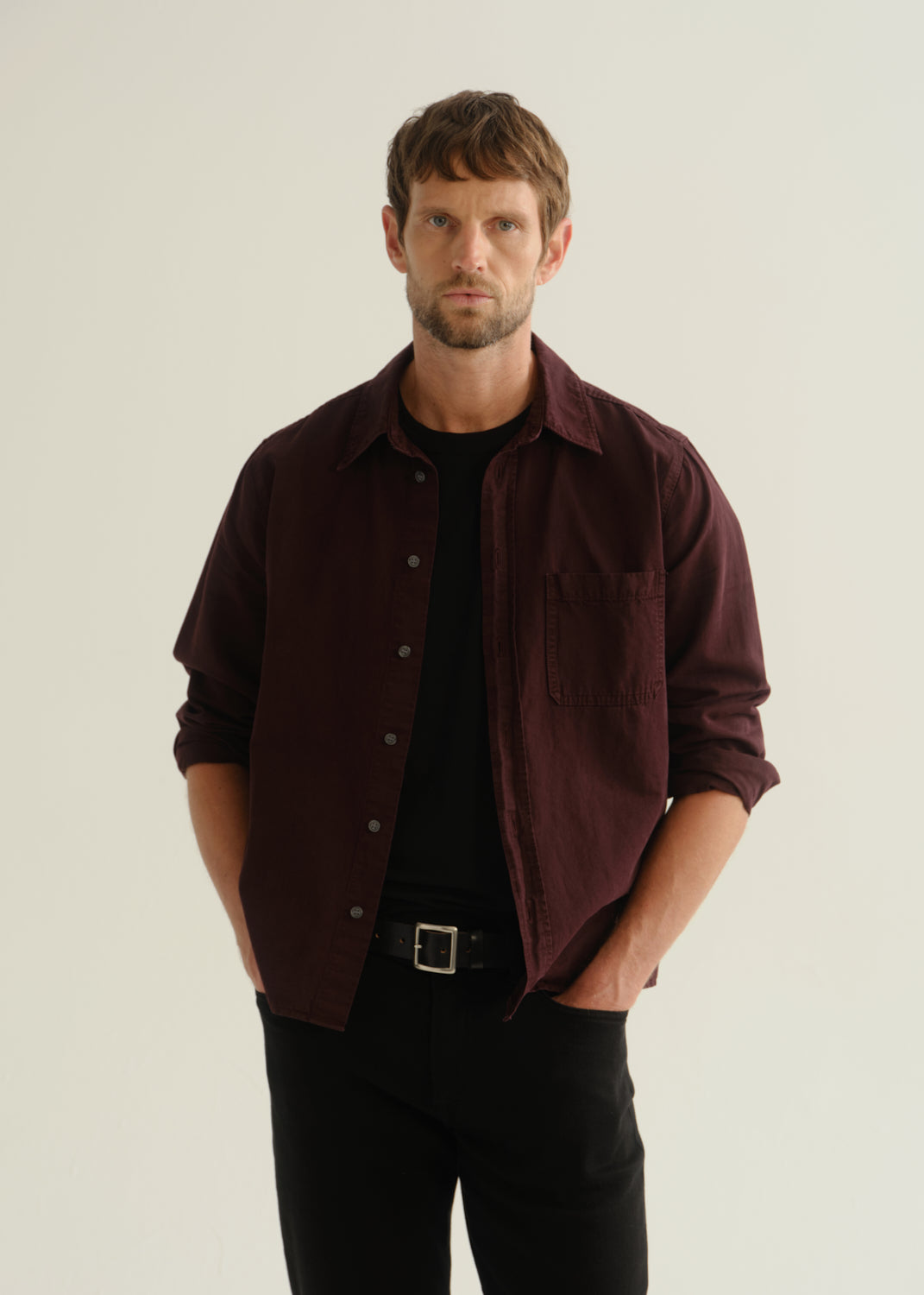 Person wearing a dark burgundy button-up shirt over a black shirt with black pants, front cropped view on a light grey background.