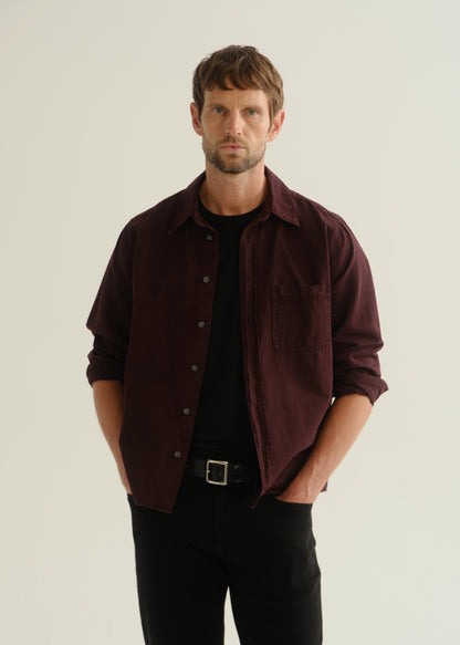 Person wearing a dark burgundy button-up shirt over a black shirt with black pants, front cropped view on a light grey background.