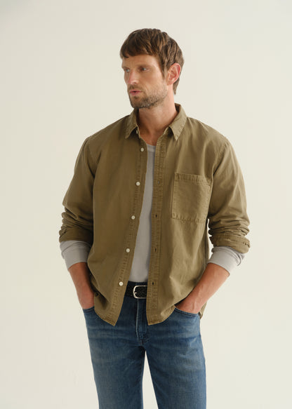 Person wearing an olive khaki long sleeve button-up shirt, a white t-shirt, and blue jeans, front cropped view on a light grey background.