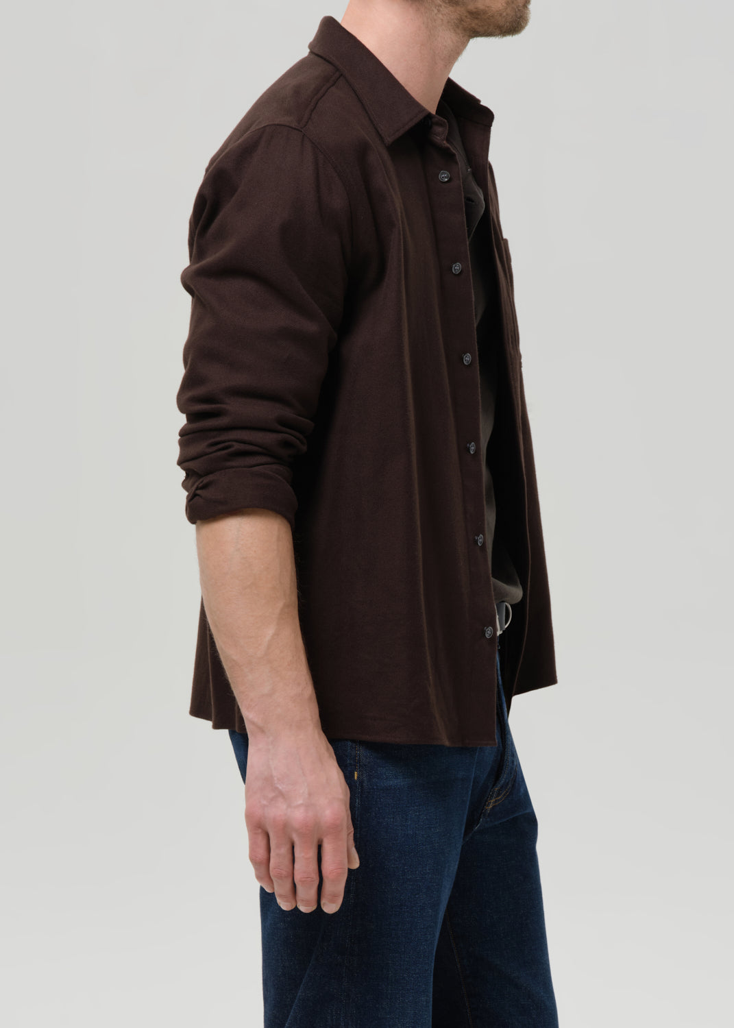 Man wearing a brown button-up shirt and blue jeans on a grey background