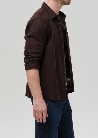 Man wearing a brown button-up shirt and blue jeans on a grey background