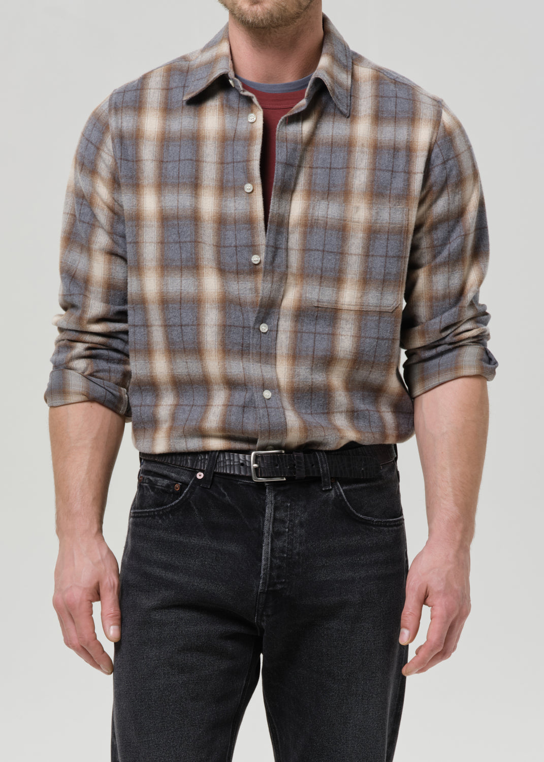 Man wearing a plaid shirt and dark jeans on a grey background