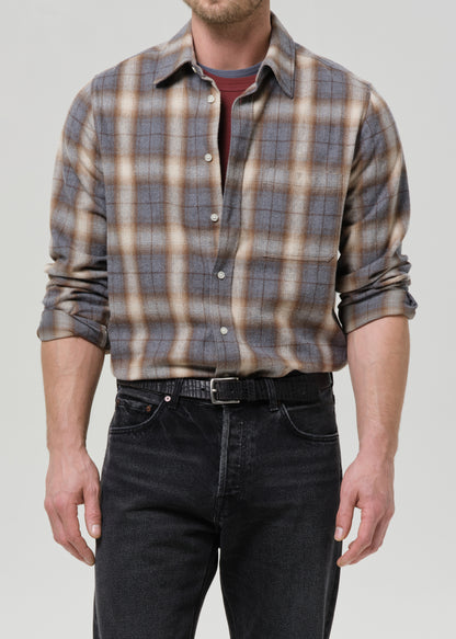 Man wearing a plaid shirt and dark jeans on a grey background