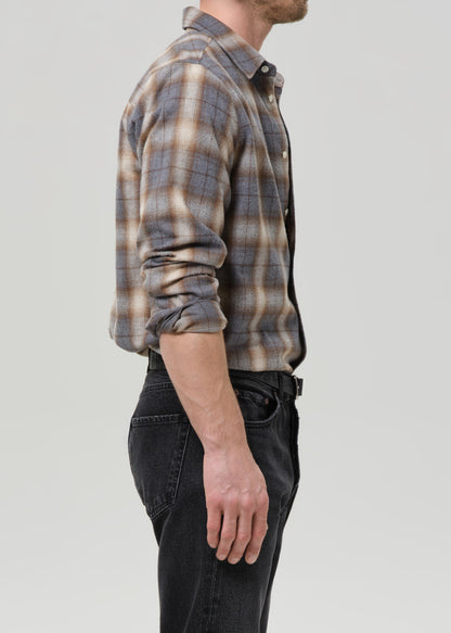 Person wearing a plaid shirt and dark pants on a grey background