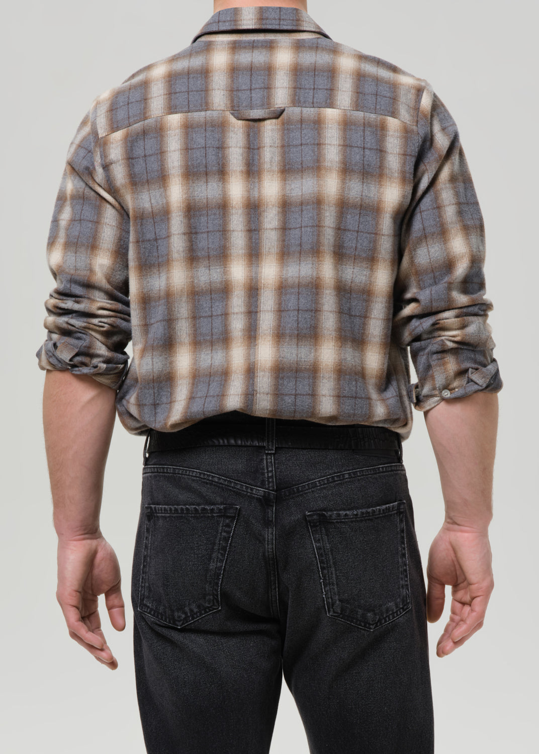 Person wearing a plaid shirt and dark jeans on a grey background