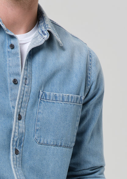 Close-up of a person wearing a light blue denim shirt on a grey background