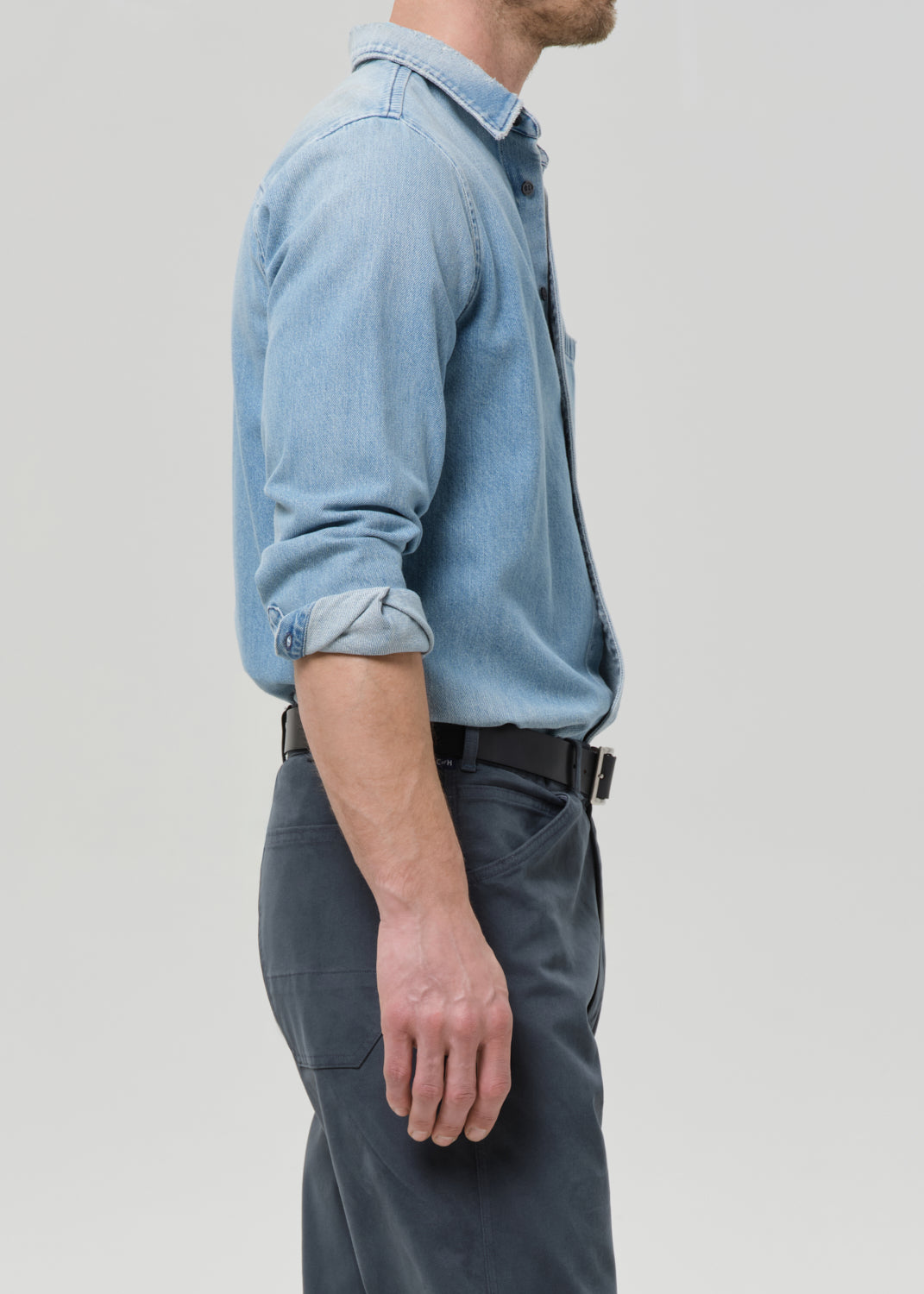 Person wearing a light blue denim shirt and dark pants on a grey background