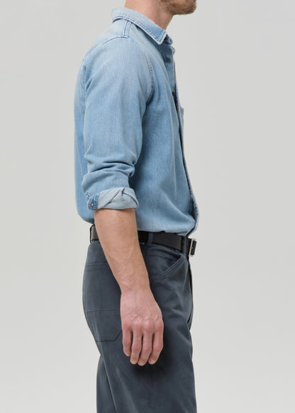 Person wearing a light blue denim shirt and dark pants on a grey background