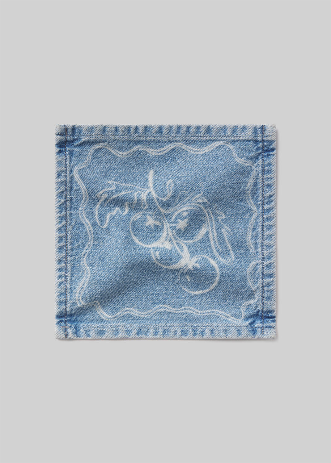 Denim cocktail napkin with tomatoes embroidered design on a light gray background