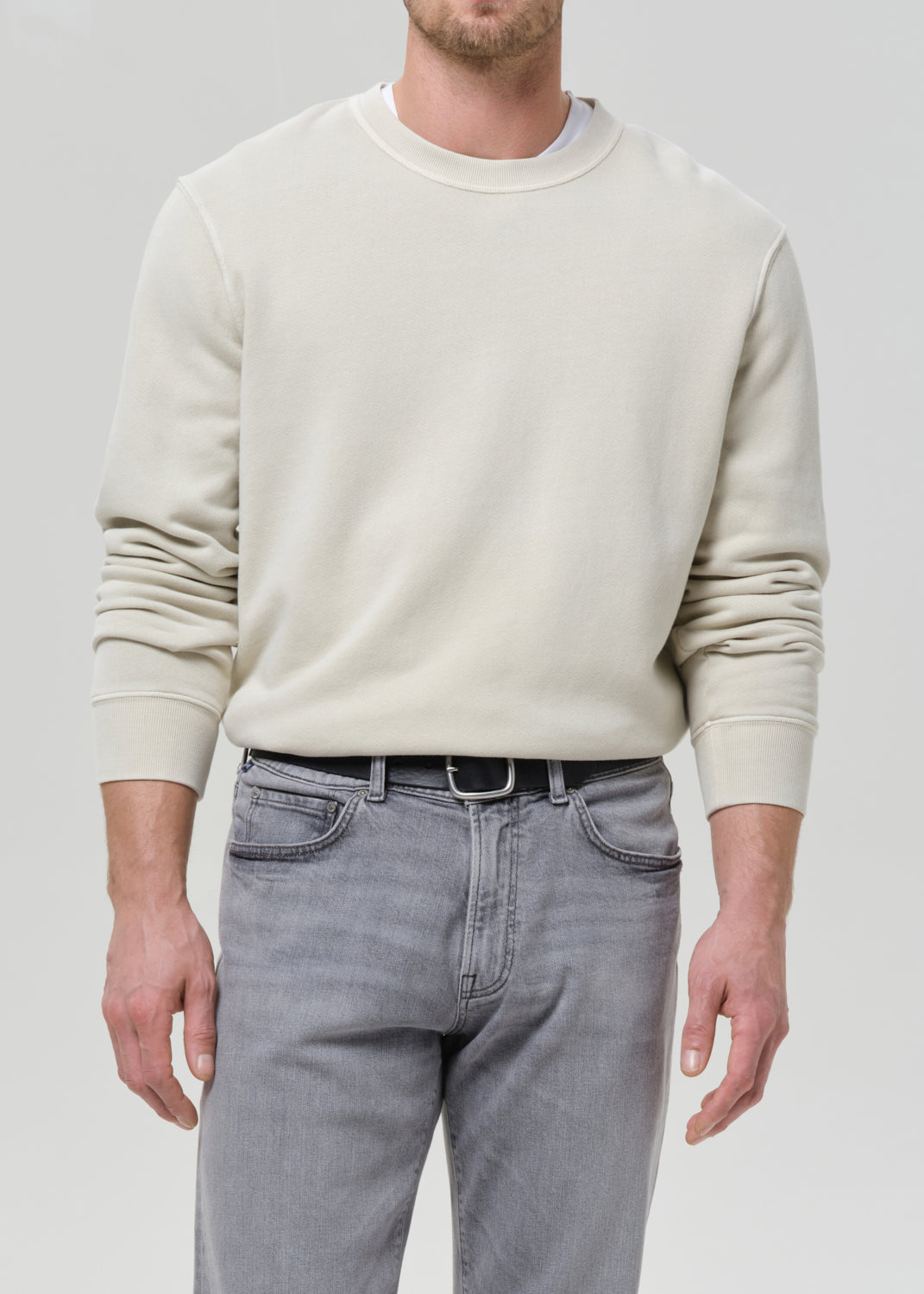 Person wearing a cream crewneck sweatshirt with light grey straight leg jeans on a grey background.
