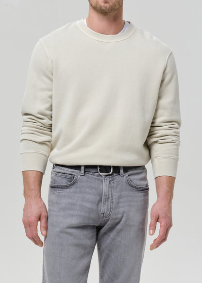 Person wearing a cream crewneck sweatshirt with light grey straight leg jeans on a grey background.
