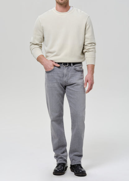 Person wearing a cream crewneck sweatshirt with light grey straight leg jeans on a grey background.