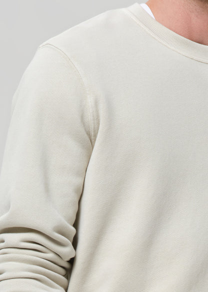 Close-up of a cream crewneck sweatshirt on a grey background.