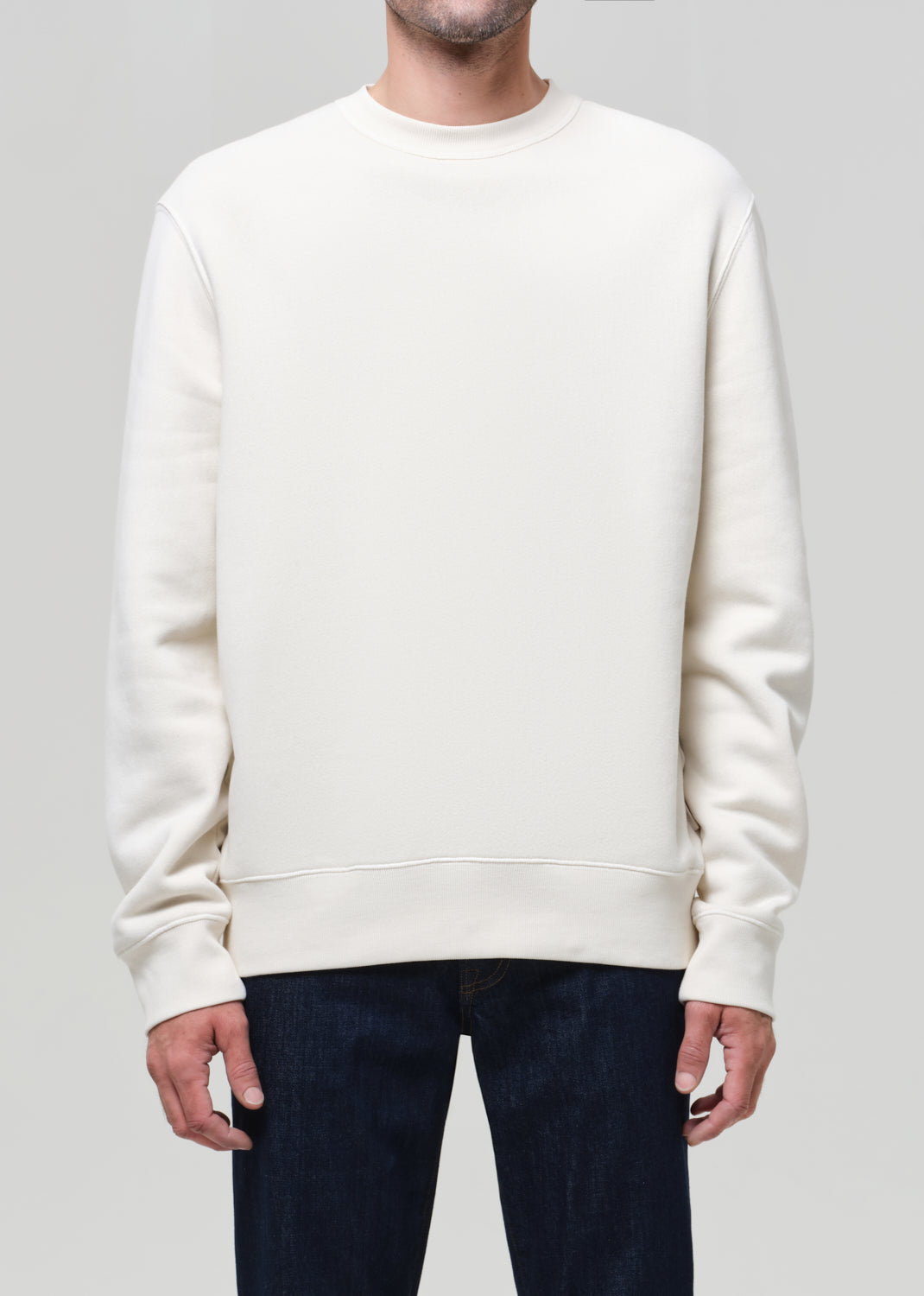 Person wearing a plain white sweatshirt and dark pants on a light gray background