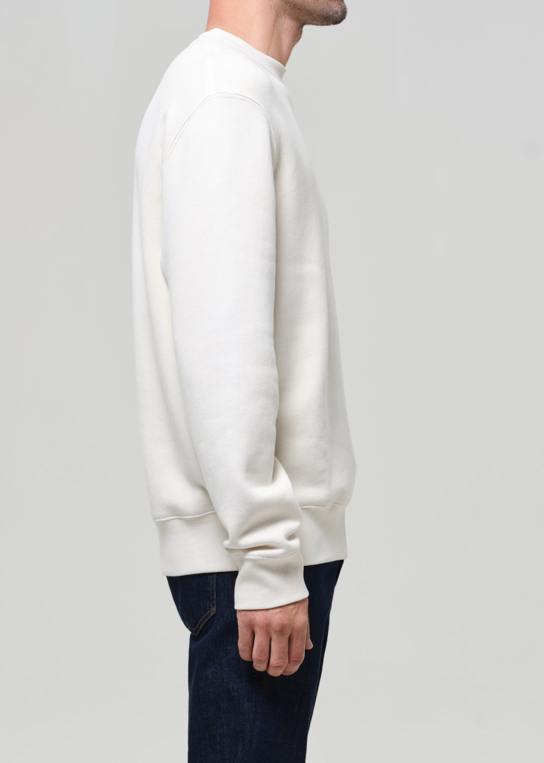 Person wearing a white sweatshirt and dark pants on a light gray background