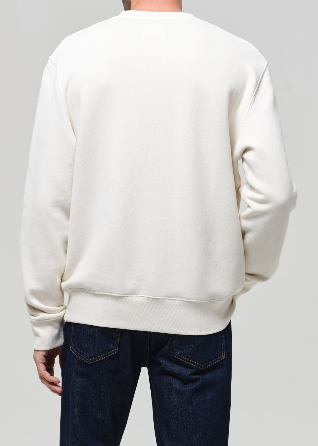 Person wearing a plain white sweatshirt and dark jeans on a light gray background