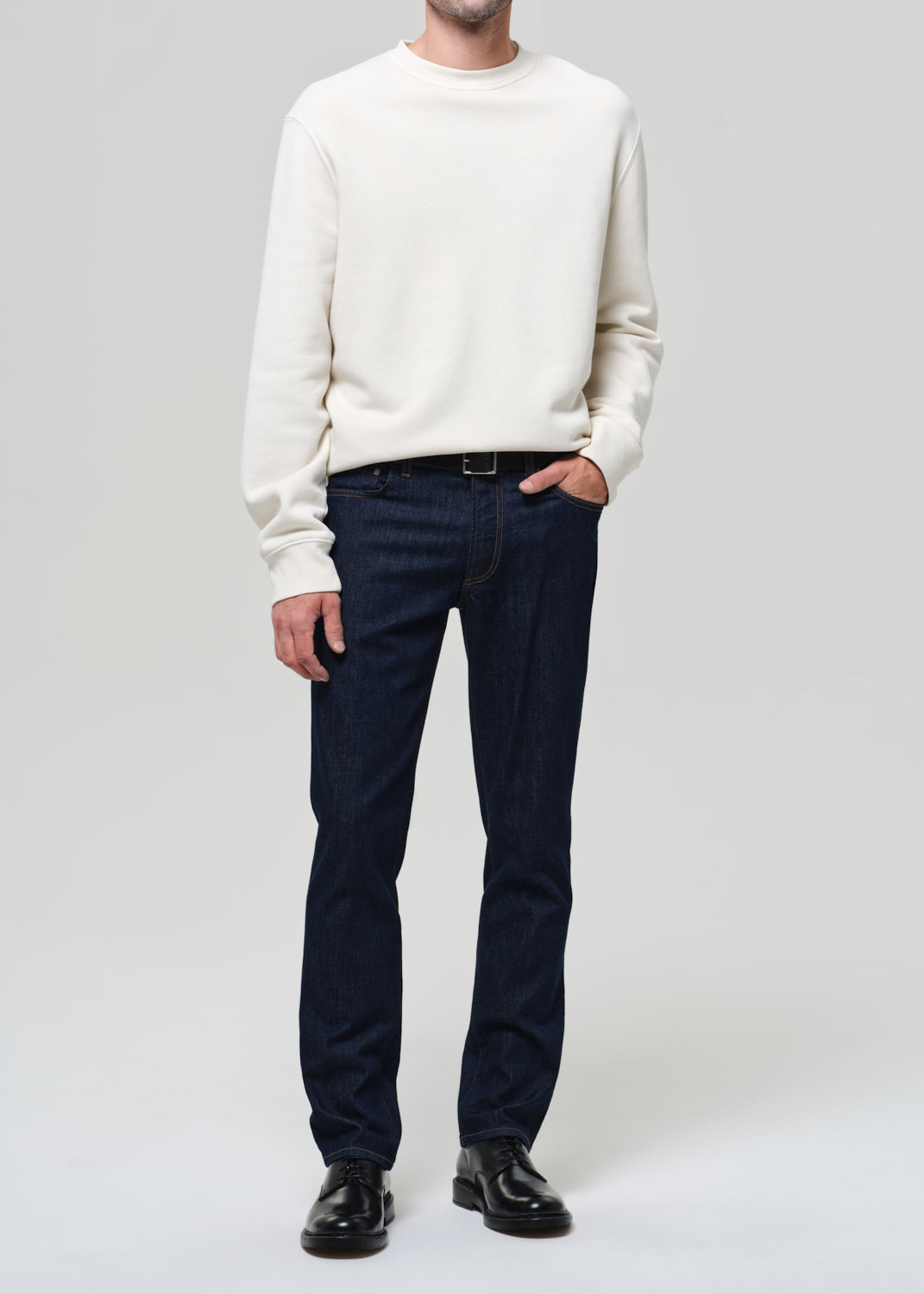 Person wearing a white sweater and dark jeans on a plain background