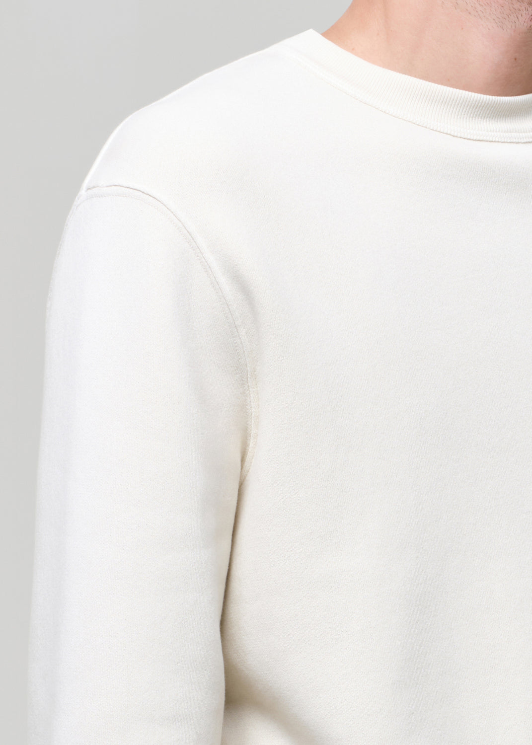 Close-up of a person wearing a plain white long-sleeve shirt against a gray background