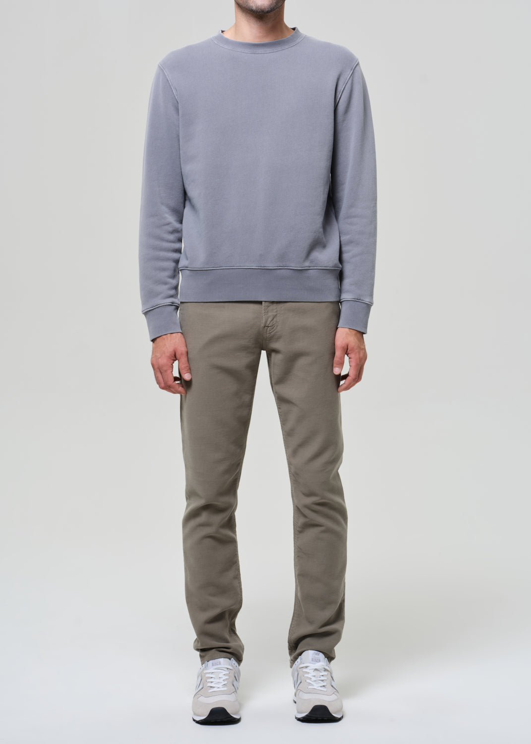 Person wearing a gray sweatshirt and beige pants on a white background