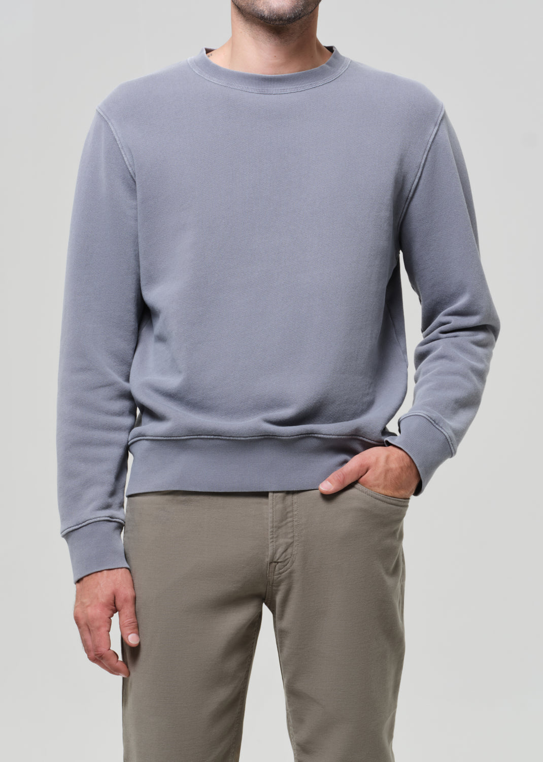 Person wearing a gray sweatshirt and beige pants on a plain background