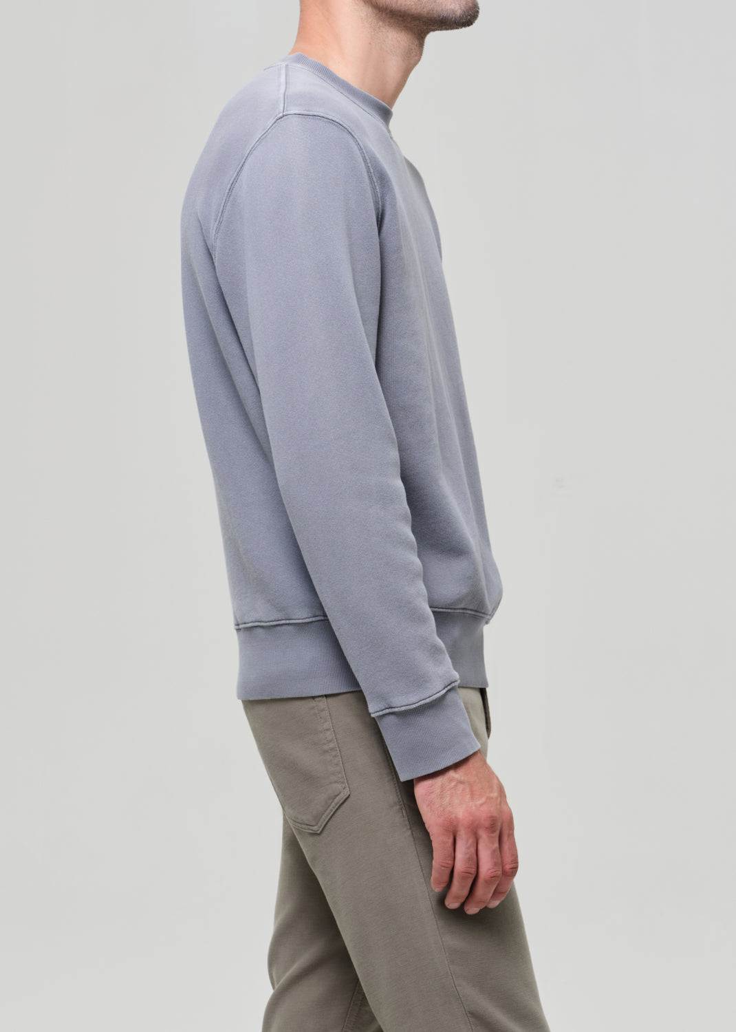 Person wearing a light gray sweatshirt and beige pants on a plain background