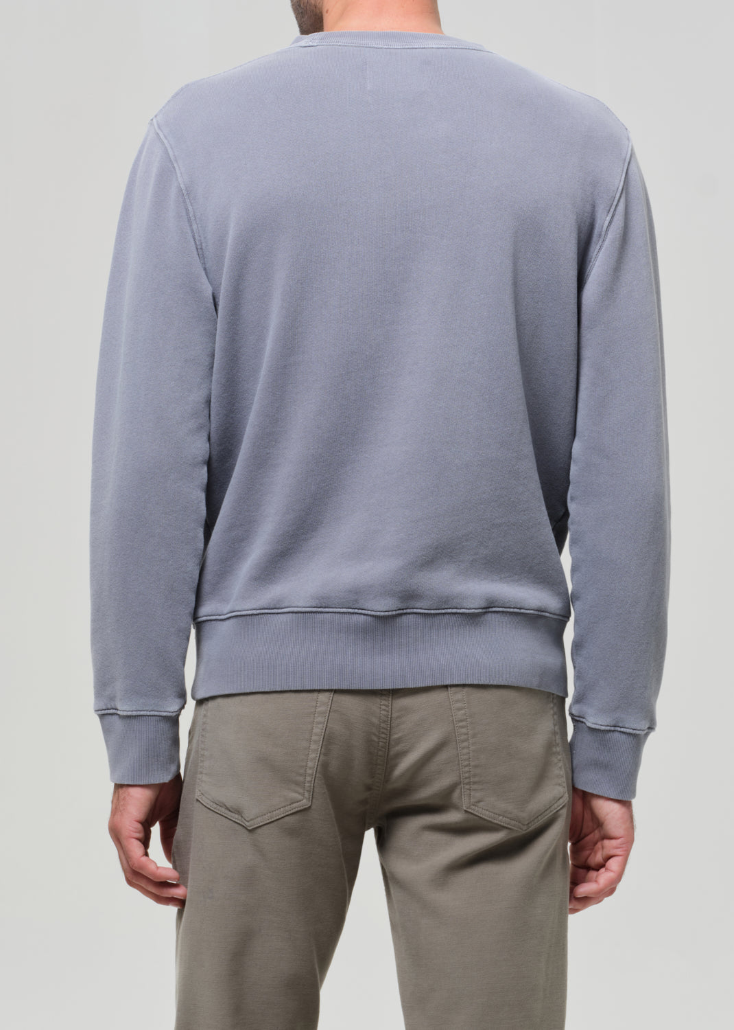 Person wearing a light gray sweatshirt and beige pants on a plain background