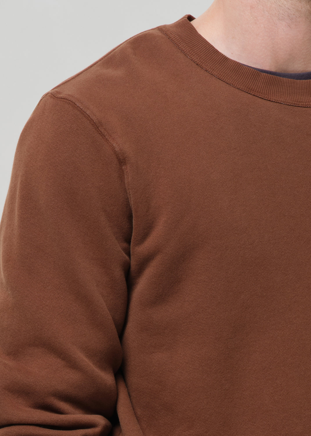 Close-up of a brown crewneck sweatshirt on a grey background.