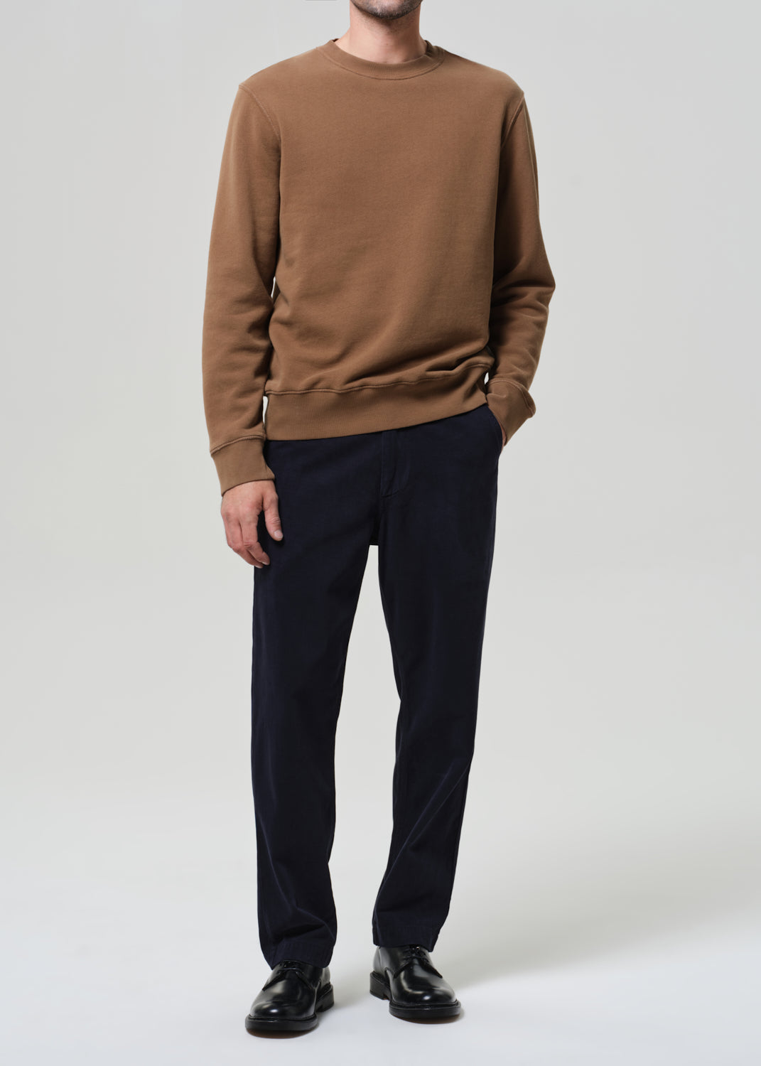 Person wearing a brown sweater and black pants on a white background