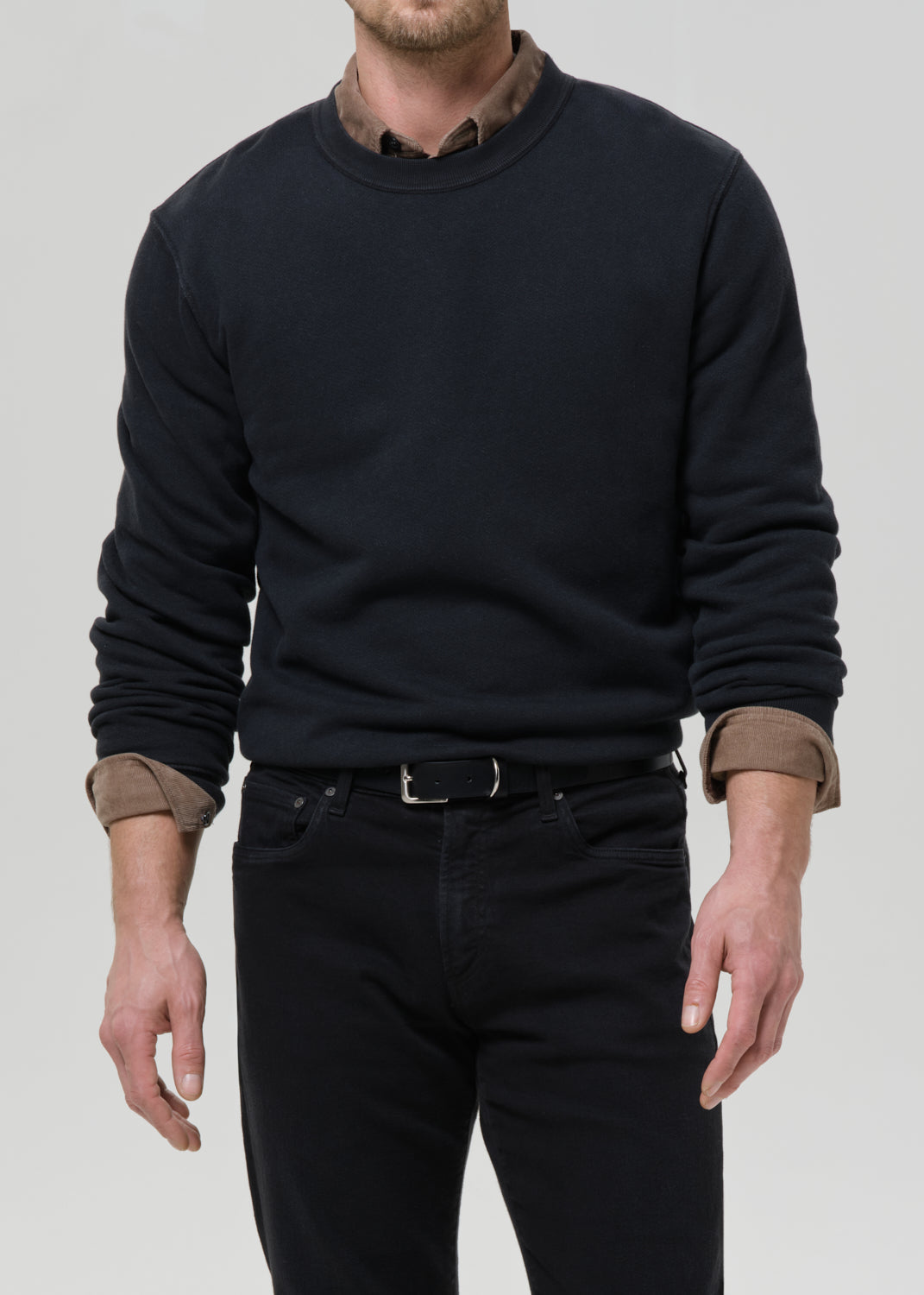 Person wearing a black crewneck sweatshirt with black straight leg jeans on a grey background.